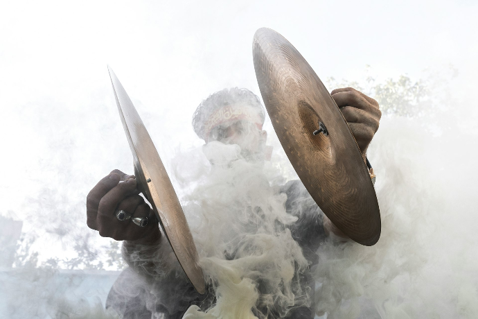 A person holding cymbals emerges from thick smoke.